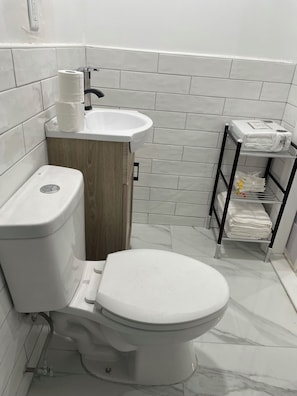 A bathroom with a toilet, sink, and a shelf with towels. - Private room in tiny home in Brooklyn, New York (Brooklyn)