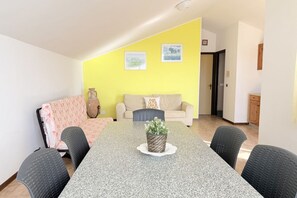 Zona pranzo con tavolo in granito, quattro sedie, un divano e una parete colorata di giallo.