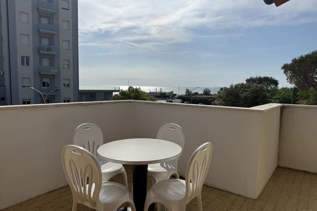 A balcony with a round table and four chairs, overlooking a cityscape with buildings and a body of water.