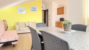 A living room with a sofa, a dining table with chairs, a small kitchen area, and a yellow wall with pictures. - M470 - Marcelli, three-room apartment with sea view (Marcelli)