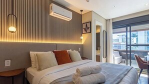 A hotel room with a bed, bedside tables, an air conditioning unit, a wall-mounted light, and a view of the city through large windows. - House in Condo. w/ Garage in Salvador Tstedf0401 (Salvador)