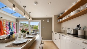 A modern kitchen with a large window, wooden shelves, and a dining area with a view. - Hydrangea House -  a managed house that sleeps 10 guests  in 4 bedrooms (Hythe)