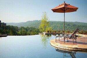 Una piscina con vistas a una cadena montañosa boscosa, una tumbona y una sombrilla.