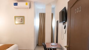 Ein Hotelzimmer mit einem Bett, einem Schreibtisch mit Stuhl, einem an der Wand befestigten Fernseher und einer Tür mit der Nummer 302.