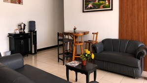 Ein Wohnzimmer mit einer Couch, einem Esstisch mit Stühlen, einer Kaffeemaschine und einem Bild an der Wand.