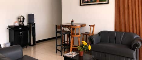 A living room with a sofa, a dining table with chairs, a coffee machine, and a painting on the wall.