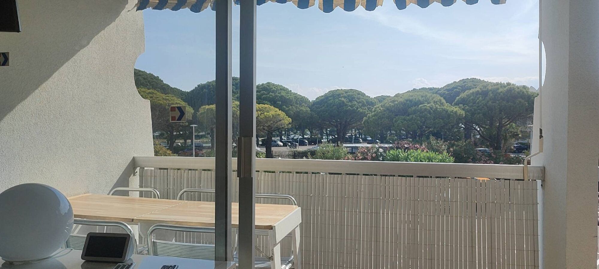 A balcony with a table and chairs, a laptop, and a view of a forested area.
