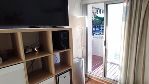 Quarto com televisão em prateleira de madeira, um armário pequeno e porta de vidro deslizante para uma varanda.