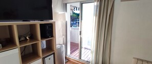 A room with a television on a wooden shelf, a small cabinet, and a sliding glass door leading to a balcony. - Apartment with separate bedroom, sleeps 5 and south-facing terrace (Le Grau-du-Roi)