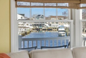 A view through a window of a waterfront property with a dock, boats, and residential buildings. - Cozy Coastal Luxury Home w/ Dock + Panoramic Views (Stafford Township)