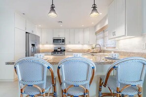 A modern kitchen with white cabinets, a central island with chairs, and pendant lighting. - Cozy Coastal Luxury Home w/ Dock + Panoramic Views (Stafford Township)