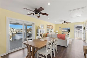 A spacious living area with a dining table, white chairs, a sofa, and a balcony with a view of buildings and water. - Cozy Coastal Luxury Home w/ Dock + Panoramic Views (Stafford Township)