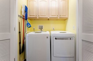 A laundry room with two white dryers, wooden cabinets above, and a blue mop on the wall. - Cozy Coastal Luxury Home w/ Dock + Panoramic Views (Stafford Township)