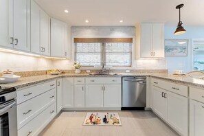 Een moderne keuken met witte kasten, een roestvrijstalen vaatwasser en een raam met houten zonwering.