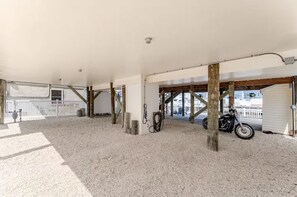 A covered outdoor area with a gravel floor, wooden beams, a motorcycle, and a white fence. - Cozy Coastal Luxury Home w/ Dock + Panoramic Views (Stafford Township)