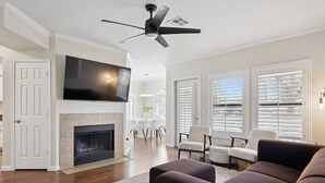 Una sala de estar con chimenea, ventilador de techo, televisor de pantalla plana y comedor con mesa y sillas.
