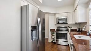 Una cocina moderna con electrodomésticos de acero inoxidable, armarios blancos y piso de madera.