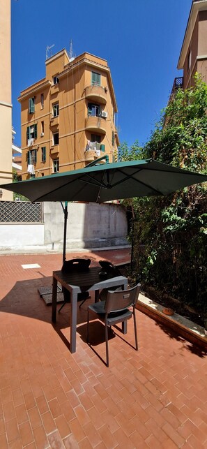 An outdoor patio with a table and chairs, a green umbrella, and a building in the background. - Tranquility and Comfort near Trastevere (Roma)