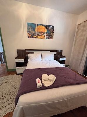 Een hotelkamer met een bed, twee nachtkastjes, een groot schilderij en een raam met gordijnen.