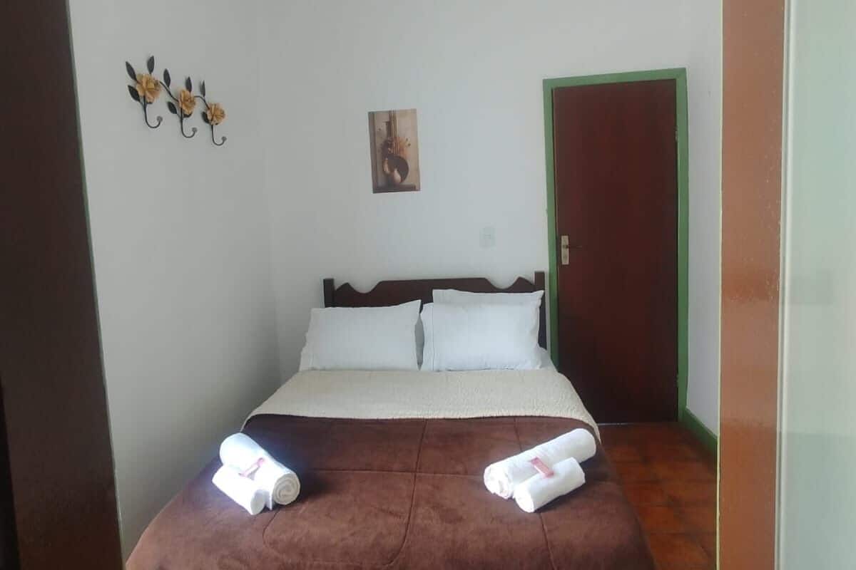 A bedroom with a bed, pillows, a towel, a painting, and a door.