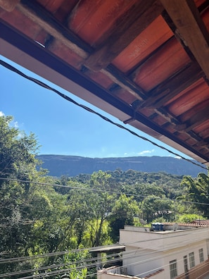 Uitzicht vanaf een overdekt balkon met houten plafond, uitkijkend over een weelderig groen landschap en verre bergen.
