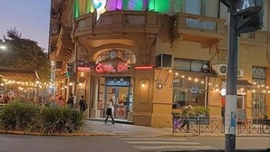 Un edificio histórico con una entrada iluminada en verde, un letrero de neón y vista a la calle.