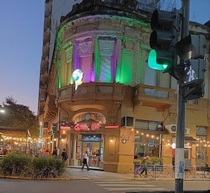 A historic building with a green-lit entrance, a neon sign, and a street view.