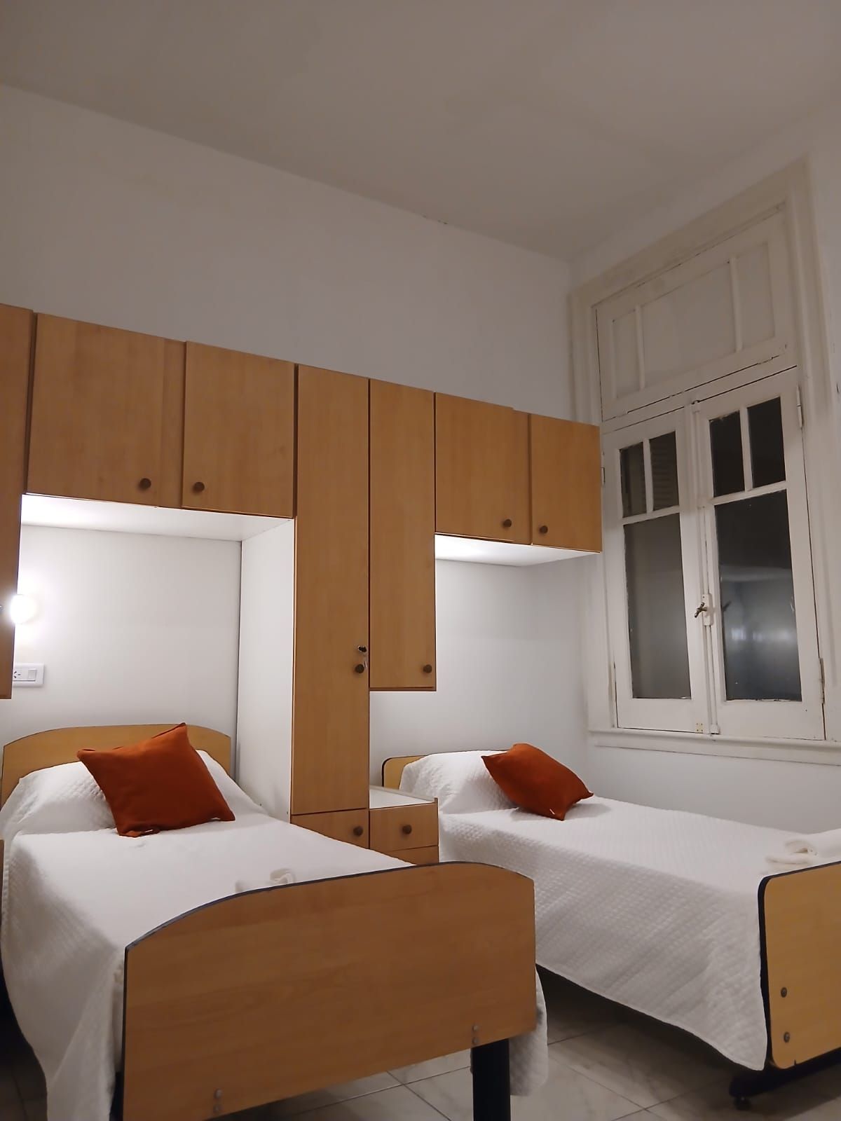 Una habitación con dos camas individuales, cabeceros de madera, ropa de cama blanca y una ventana con persianas.