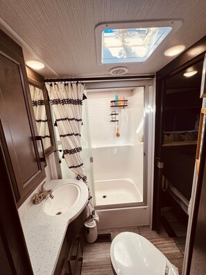 A compact RV bathroom with a shower, toilet, and sink.
