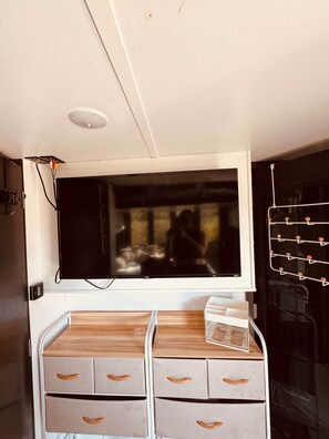 A room with a large flat-screen TV mounted on the wall, a wooden cabinet with drawers, and a white ceiling with a recessed light fixture.