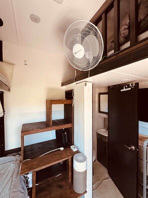 A compact room with a bunk bed, a standing fan, a small trash bin, and a door leading to a bathroom.