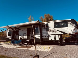 A large RV with a covered porch, a ladder, and a blue bean bag chair.