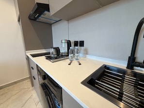 A modern kitchen with a built-in dishwasher, a coffee maker, and two water bottles on the counter. - 413 Tara-jre Jabal Al Lweibdeh With Stunning View (Amman)