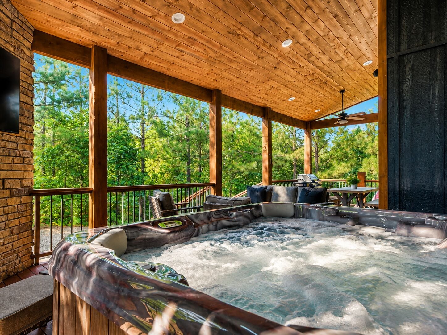 A hot tub area with a wooden ceiling and a view of a forest.