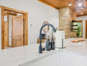 A modern kitchen with a curved faucet, a stone accent wall, and a wooden door. - NEW! Tipi, Hot Tub, Arcade Games, Fire Pit, King Beds & Near Hochatown (Broken Bow)
