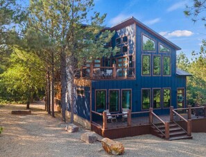 A multi-story wooden cabin with a balcony, surrounded by trees. - NEW! Tipi, Hot Tub, Arcade Games, Fire Pit, King Beds & Near Hochatown (Broken Bow)