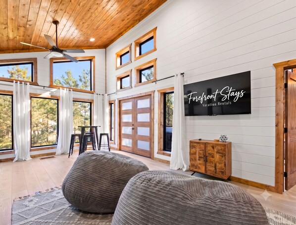 A spacious room with large windows, a ceiling fan, and a television displaying 'Forefront Stays Vacation Rentals'. - NEW! Tipi, Hot Tub, Arcade Games, Fire Pit, King Beds & Near Hochatown (Broken Bow)