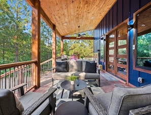 A covered outdoor seating area with a wooden ceiling, a sofa, and a table with a plant. - NEW! Tipi, Hot Tub, Arcade Games, Fire Pit, King Beds & Near Hochatown (Broken Bow)