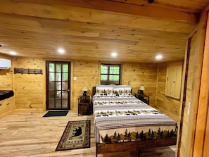 Ein Schlafzimmer einer Holzhütte mit einem Bett, zwei Nachttischen, einem Fenster, einer Tür und einem Kleiderständer.