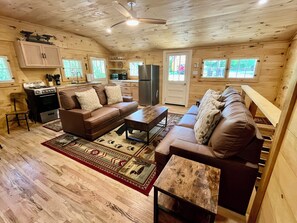 Ein gemütliches Blockhaus-Interieur mit Küchenzeile, zwei Sofas, einem Couchtisch und einem Esstisch.