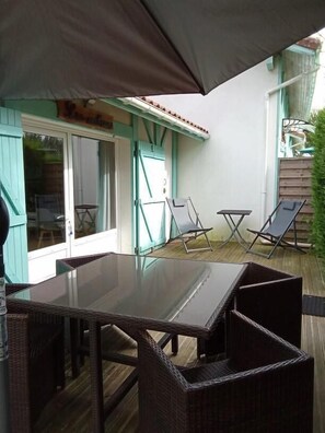 An outdoor patio with a glass table and wicker chairs, a covered area, and a sliding glass door leading to a room. - LES EMBRUNS - VIELLE SAINT GIRONS (VIELLE SAINT GIRONS)