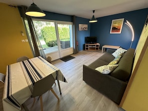 A living room with a sofa, a dining table with chairs, a television, and a sliding glass door leading to an outdoor area. - LES EMBRUNS - VIELLE SAINT GIRONS (VIELLE SAINT GIRONS)