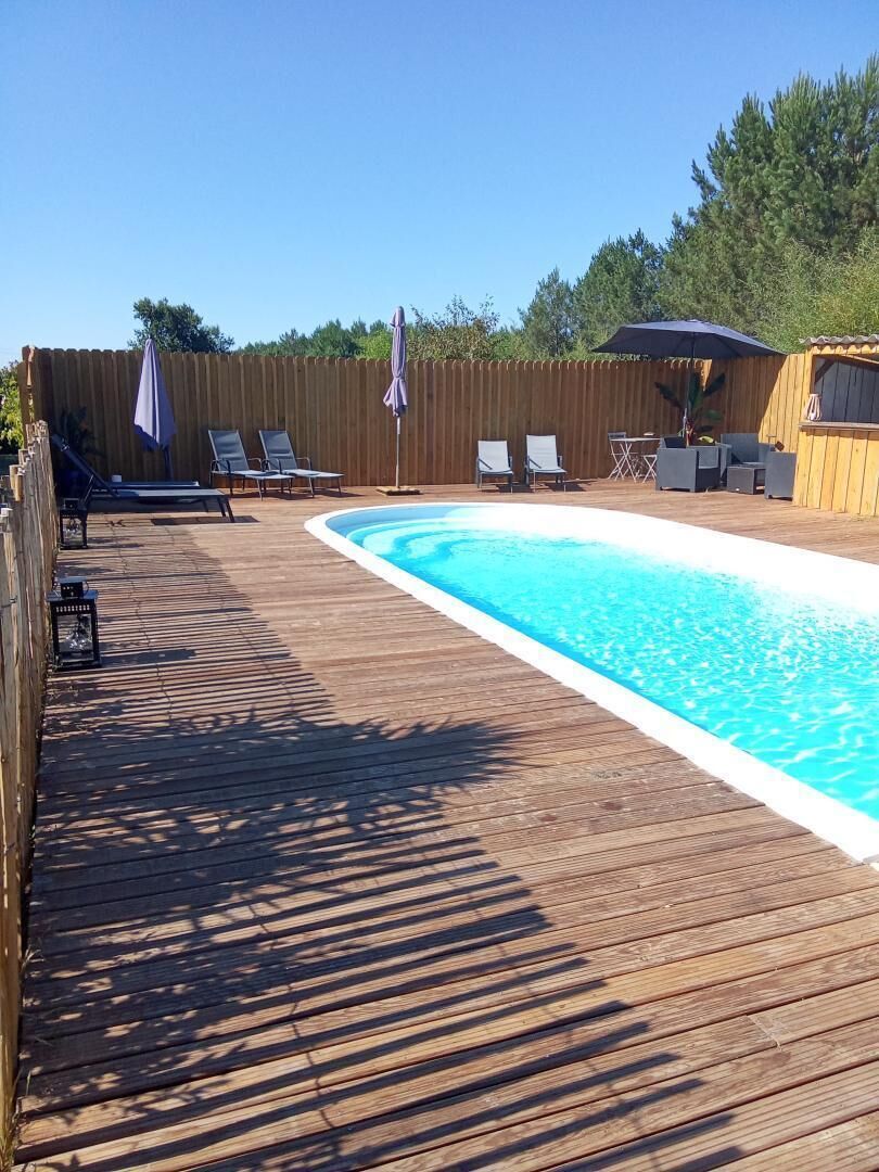 Una terraza de madera con piscina, sillas de descanso y sombrillas.