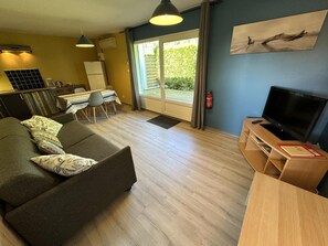 A living room with a sofa, a TV, a dining table with chairs, a fireplace, and a large window. - LES EMBRUNS - VIELLE SAINT GIRONS (VIELLE SAINT GIRONS)