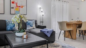 Ett modernt vardagsrum med en soffa, ett soffbord, en orkidé och en matplats med stolar och ett bord.