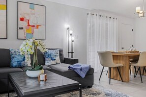 A modern living room with a sofa, coffee table, orchid plant, and a dining area with chairs and a table. - Beautiful updated home in the heart of The Colony (The Colony)