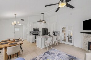 A modern kitchen with white cabinets, a central island, and a dining area with a wooden table and chairs. - Beautiful updated home in the heart of The Colony (The Colony)