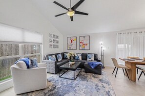 A modern living room with a sectional sofa, a coffee table, and a dining area with a wooden table and chairs. - Beautiful updated home in the heart of The Colony (The Colony)