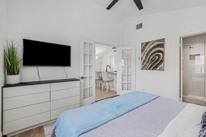 A bedroom with a bed, a TV mounted on the wall, a desk with a chair, and a shower area. - Beautiful updated home in the heart of The Colony (The Colony)