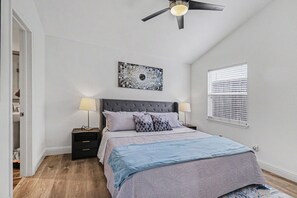 A bedroom with a bed, two bedside tables, a ceiling fan, a window with blinds, and a wall-mounted artwork. - Beautiful updated home in the heart of The Colony (The Colony)